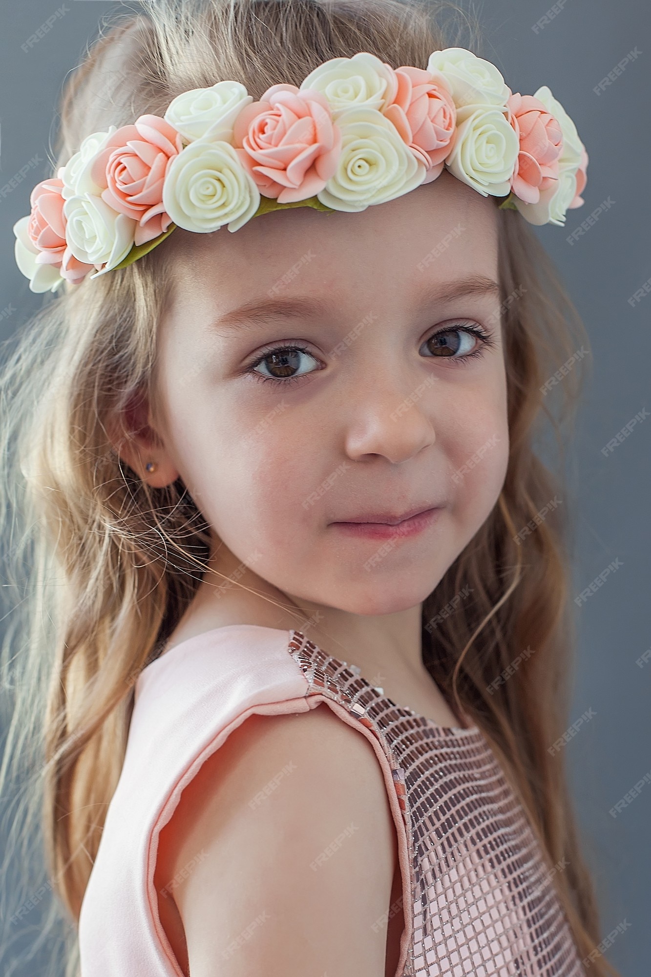 Niña con un vestido y una corona de flores la cabeza se para y mira a la cámara. | Foto Premium