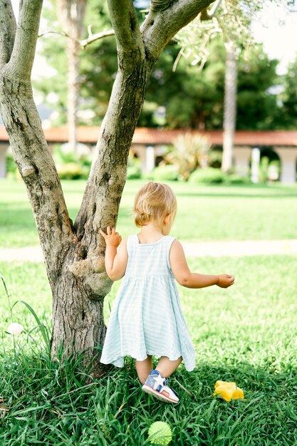 Niña en un vestido está apoyado en un árbol en el parque