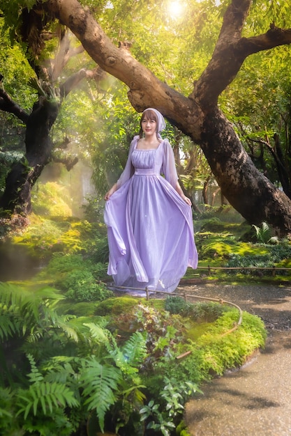 Foto niña en un vestido de princesa está en un bosque profundo misterioso con árboles flores y cascadas en la espalda