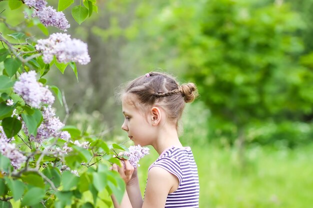 Niña con vestido de rayas que huele las flores Syringa o Lila en el parque de la primavera.