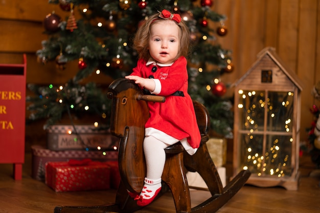 Niña en vestido rojo en caballito de madera columpio. Fiestas navideñas tiempo fabuloso para los niños