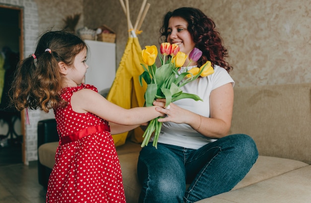 Una niña con un vestido rojo le da a una madre feliz un gran ramo de tulipanes brillantes. Un regalo para los padres.