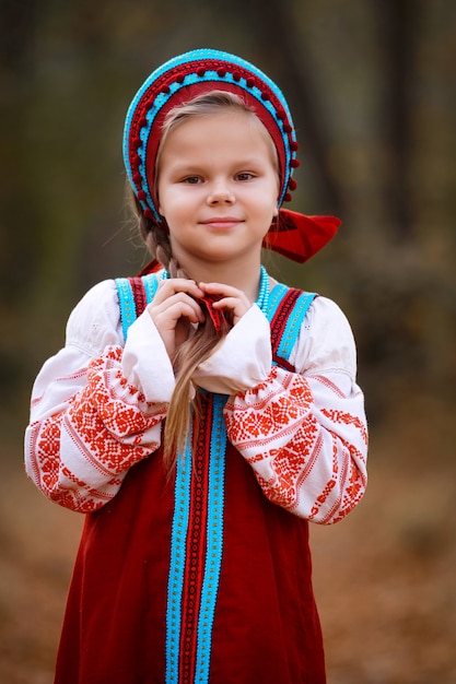 una niña con un vestido rojo se encuentra en el bosque de otoño y trenza su cabello