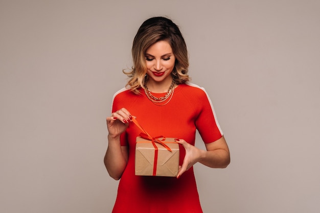 Una niña con un vestido rojo se encuentra con regalos en sus manos sobre un fondo gris