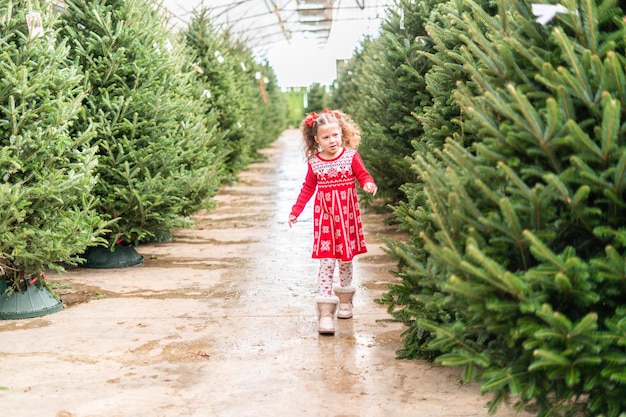 Niña de vestido rojo en la granja de árboles de Navidad.