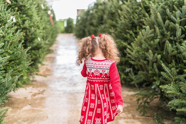 Niña de vestido rojo en la granja de árboles de Navidad.