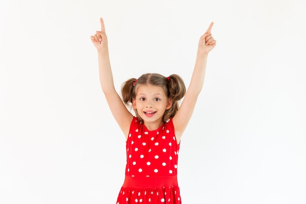 Una niña con un vestido rojo señala su anuncio sobre un fondo blanco aislado;