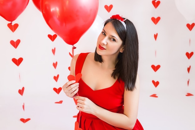 Una niña con un vestido rojo sostiene un globo con una guirnalda de corazones.