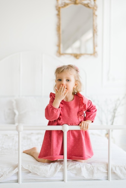 Niña en vestido rosa divirtiéndose en la cama en el dormitorio