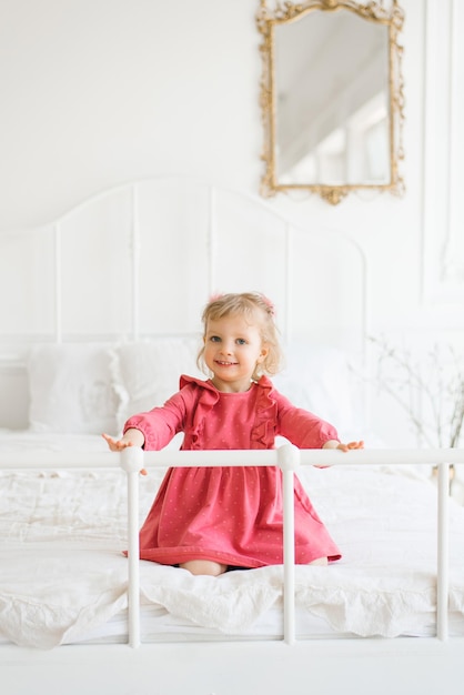 Niña en vestido rosa divirtiéndose en la cama en el dormitorio