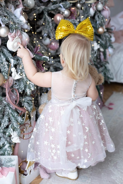 Una niña con un vestido rosa se encuentra cerca de un árbol de navidad.