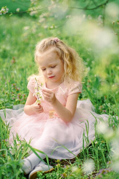 niña con un vestido rosa examina flores de primavera