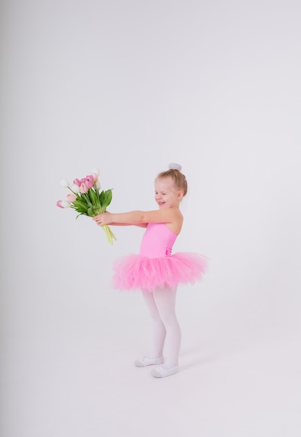 Foto niña con un vestido rosa con una falda de tutú presenta un ramo de tulipanes en una pared blanca