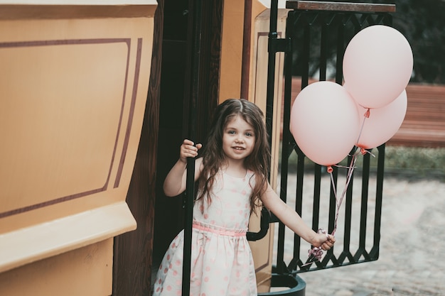 Una niña con un vestido rosa sale del tranvía con pelotas. Foto de alta calidad