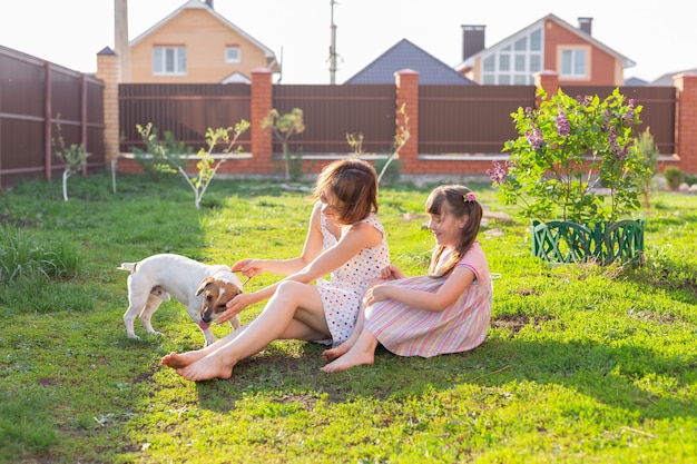 Niña en vestido rosa con su madre y perro jack russell terrier en el patio sentado en la hierba