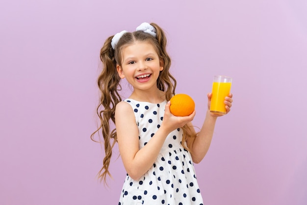 Una niña con un vestido sostiene dos naranjas en la mano Vitaminas frescas para el desayuno
