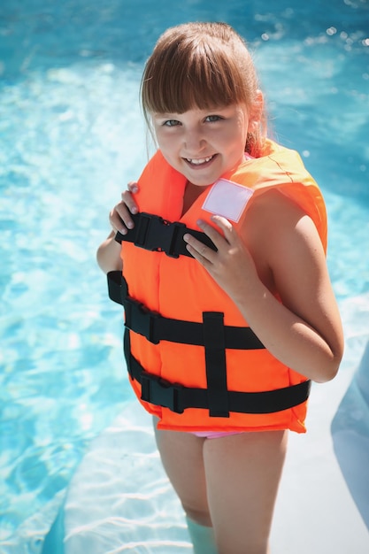 Niña vestidos de naranja chaleco salvavidas en la piscina al aire libre