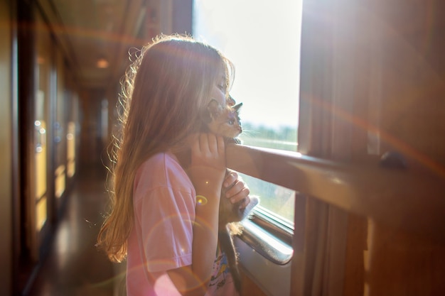 Una niña viaja en un carruaje con un gatito. Viajar con animales en tren. Un niño con un gato mira por la ventana de un tren.