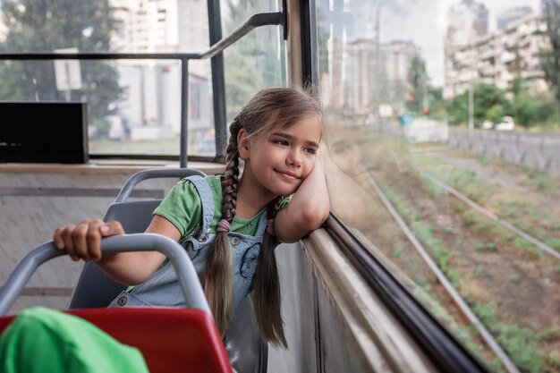 La niña viaja en un tranvía vacío y mira la ventana soñadoramente en el tranvía de la ciudad de transporte público