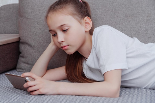 Una niña viendo un video en su teléfono mientras está acostada en el sofá