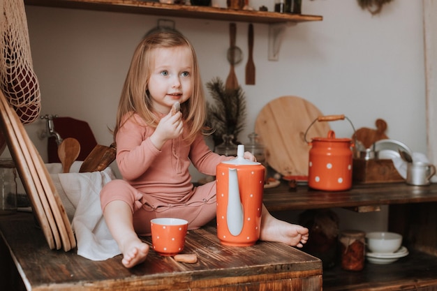 la niña vierte té en una taza de una tetera platos de cerámica roja en la cocina de madera de guisantes blancos