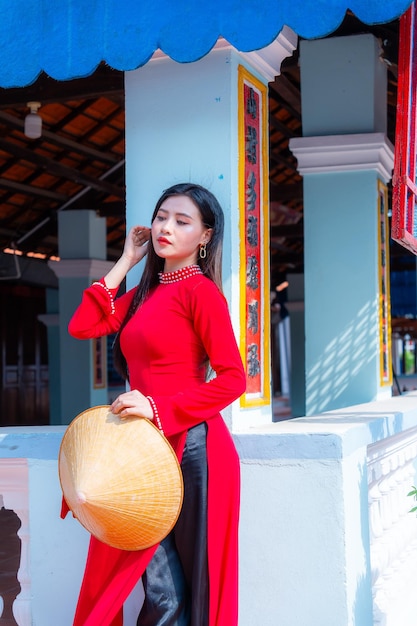 Foto niña vietnamita con vestido ao dai de pie en una casa tradicional de vietnam el texto en la foto significa mejores deseos de felicidad familiar prosperidad salud vacaciones de tet y año nuevo