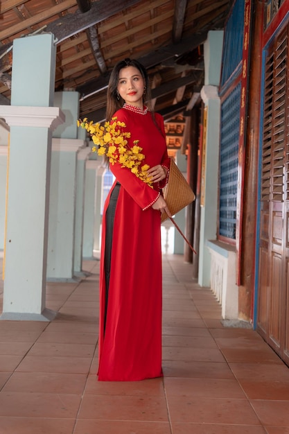 Foto niña vietnamita con vestido ao dai de pie en una casa tradicional de vietnam el texto en la foto significa mejores deseos de felicidad familiar prosperidad salud vacaciones de tet y año nuevo