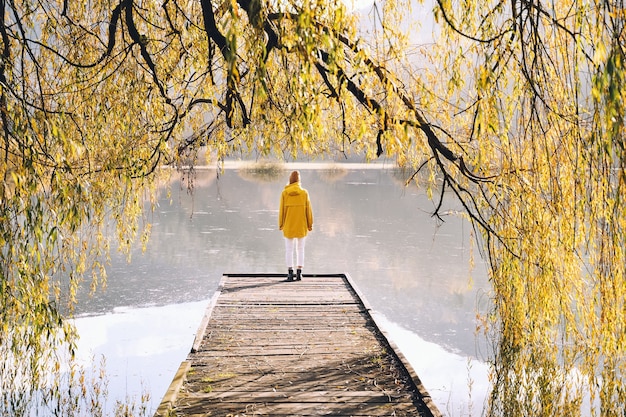 Niña vistiendo impermeable amarillo mirando el lago o estanque en la naturaleza