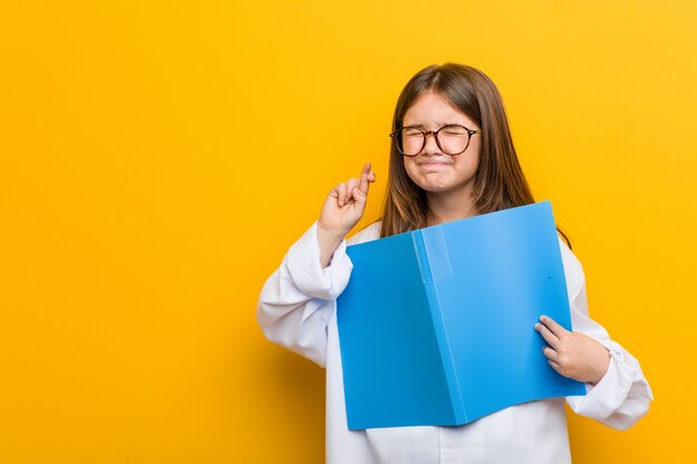 Niña vistiendo un traje de médico cruzando los dedos para tener suerte