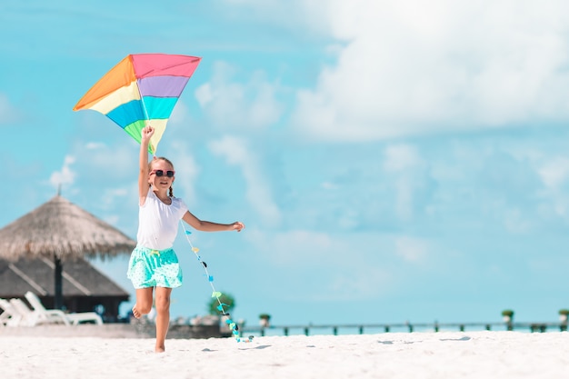 Niña volando una cometa en la playa con agua turquesa