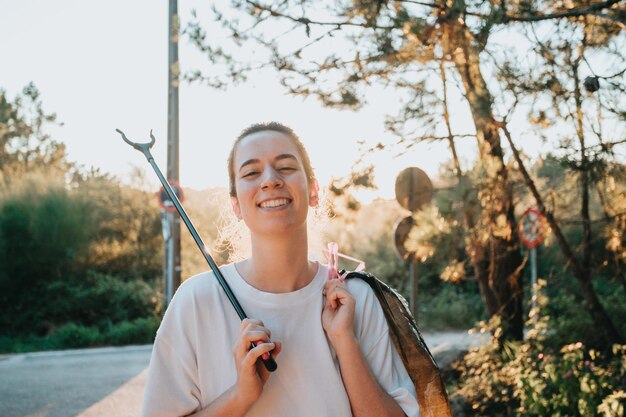 Niña voluntaria limpiando el bosque de la contaminación y los plásticos al atardecer con basura sonriendo a la cámara feliz día ecológico Naturaleza limpieza ecología concepto verde Espacio de copia ambiental