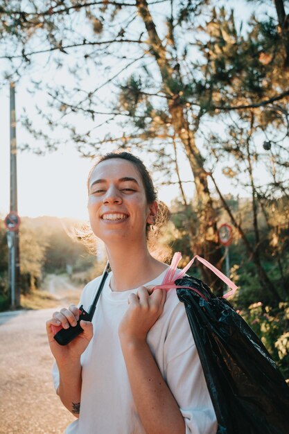 Niña voluntaria limpiando el bosque de la contaminación y los plásticos al atardecer con basura sonriendo a la cámara feliz día ecológico Naturaleza limpieza ecología concepto verde Espacio de copia ambiental