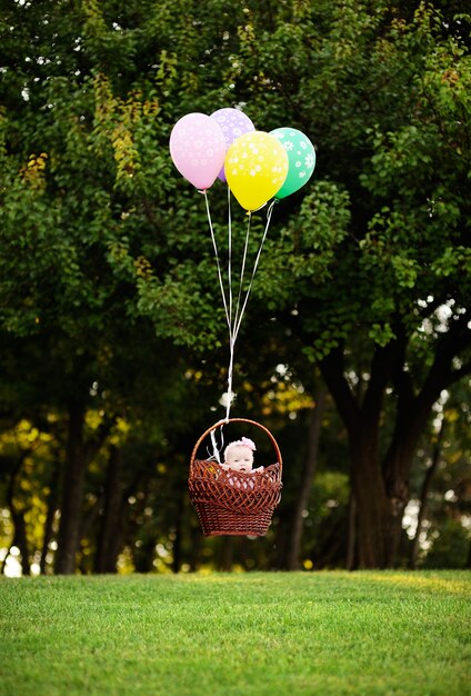 La niña vuela en globos sobre un fondo de árboles verdes.