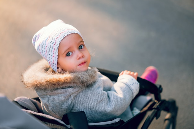 La niña se vuelve a sentar en un cochecito de bebé en un paseo por el parque.