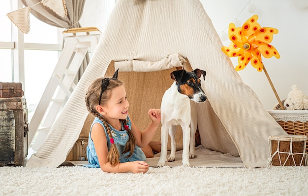 Niña en wigwam con perro fox terrier en sala de luz