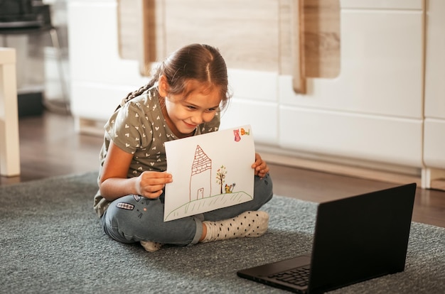 Una niña yace en la alfombra frente a la pantalla de una computadora. Comunicación en línea