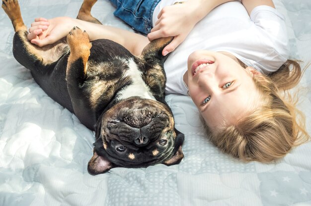 Niña yace en la cama en un abrazo con su perro de raza Bulldog Francés