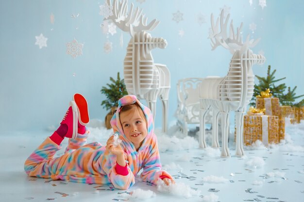 Niña en zapatillas rojas y ciervos de Navidad junto a cajas con regalos.