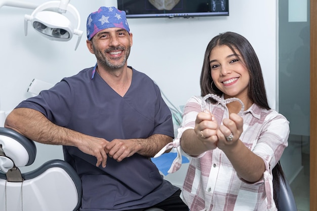 Niñas adolescentes étnicas felices mostrando alineadores de dientes cerca del dentista en la clínica