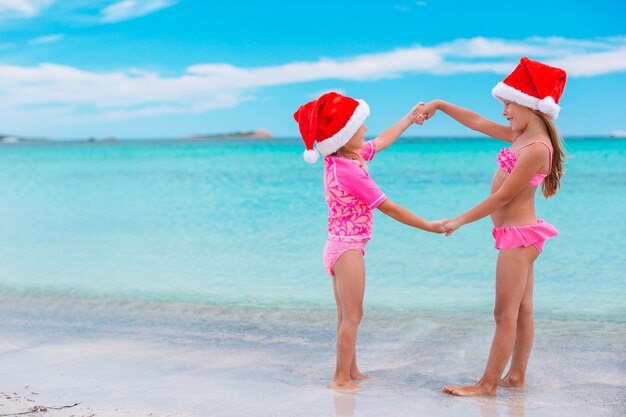 Niñas adorables con sombreros de Santa en la playa