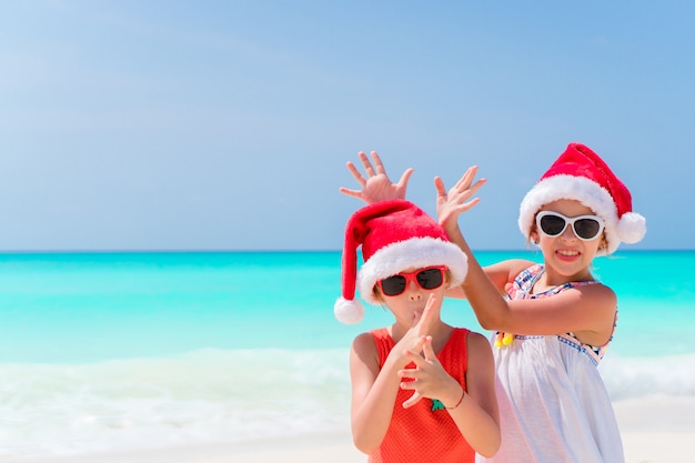 Niñas adorables con sombreros de Santa durante las vacaciones en la playa se divierten juntas