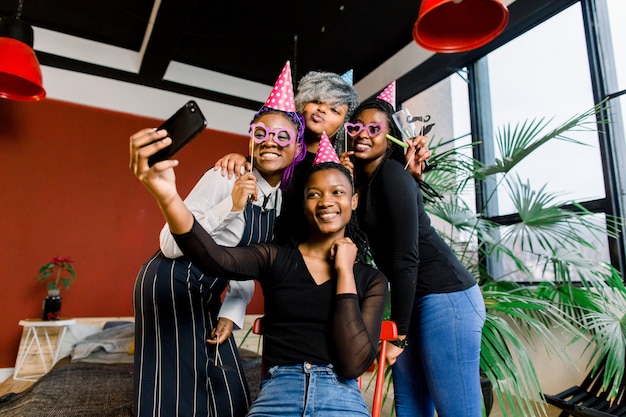 Niñas africanas felices celebran cumpleaños con sombreros y toman fotos en un teléfono inteligente