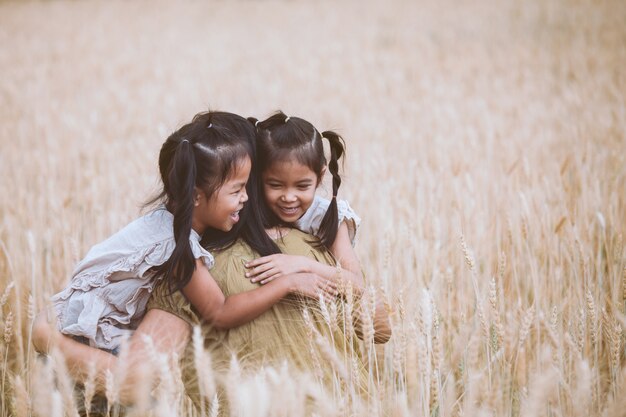 Niñas asiáticas felices del niño que abrazan a su madre y que se divierten para jugar con la madre en el campo de la cebada