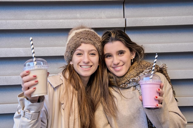 Las niñas beben un batido saludable en ropa de invierno, una mujer bonita sonríe sosteniendo una bebida de yogur de fresa