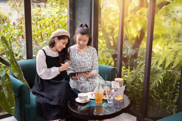 Las niñas beben café y se relajan en el café. Freelancer se comunica en el proyecto. Las niñas compran en línea en una tableta wifi. Los estudiantes estudian en internet.