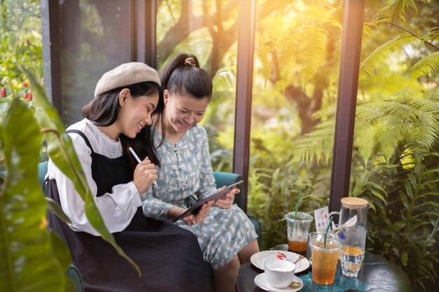 Las niñas beben café y se relajan en el café. Freelancer se comunica en el proyecto. Las niñas compran en línea en una tableta wifi. Los estudiantes estudian en internet.