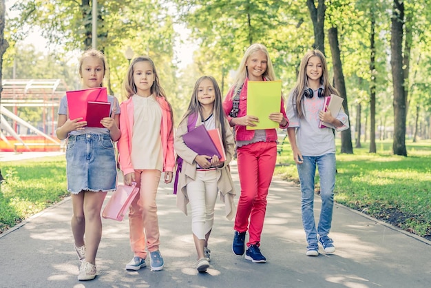 Niñas caminando en el parque con libros escolares y notas.