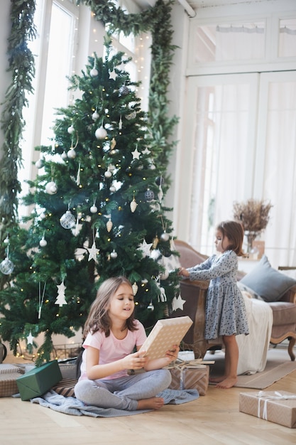 Niñas en casa durante la Navidad con árbol y regalos.