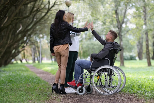 Las niñas chocan los cinco con los hombres en silla de ruedas en el parque después de la rehabilitación de amistades de primer plano