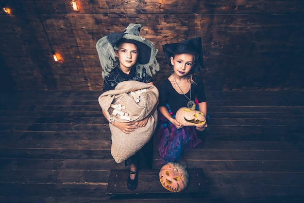 Foto niñas disfraces de brujas con calabazas y golosinas en halloween en un escenario de madera